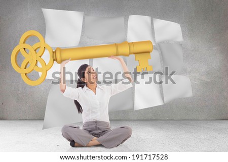 Businesswoman sitting cross legged carrying large key against floating sheets in front of grey wall