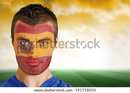 Composite image of spain football fan in face paint against football pitch under yellow sky