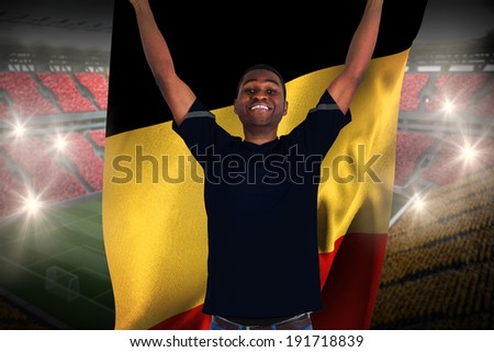 Excited football fan in black cheering holding belgium flag against vast football stadium with fans in yellow and red