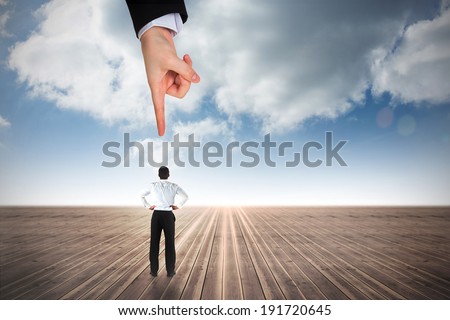 Giant hand pointing at businessman standing back to the camera with hands on hips against cloudy sky background
