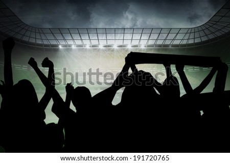 Silhouettes of football supporters against misty football stadium under spotlights