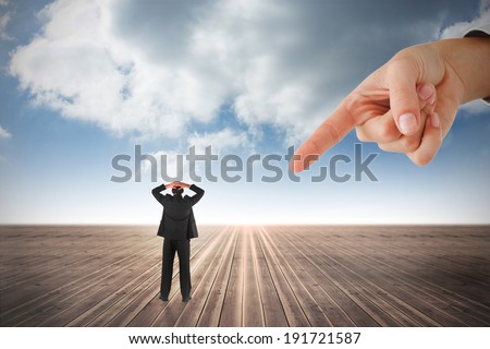 Giant hand pointing at businessman standing back to the camera with hands on head against cloudy sky background