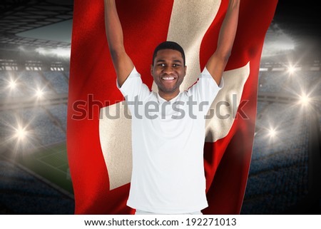 Excited handsome football fan cheering holding swiss flag against large football stadium with fans in blue