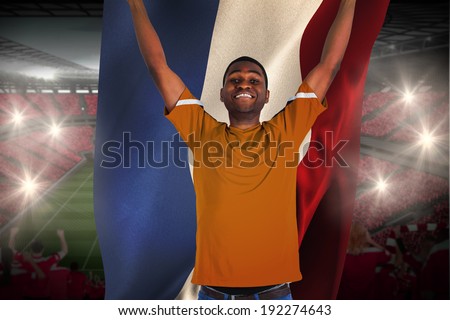 Cheering football fan in orange jersey holding netherlands flag against vast football stadium with fans in red