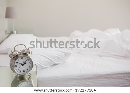 Messy bed with alarm clock on bedside table at home in bedroom