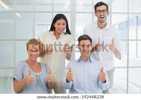Casual business team showing thumbs up to camera in the office