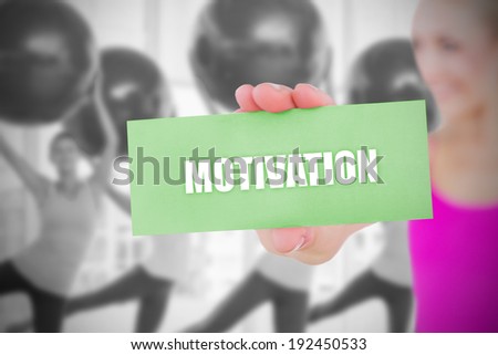 Fit blonde holding card saying motivation against fitness class in gym