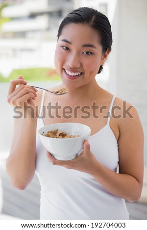 Happy woman having a bowl of cereal outside on a balcony