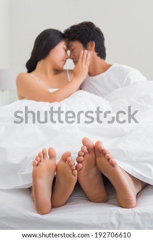 Affectionate couples feet sticking out from under duvet at home in bedroom
