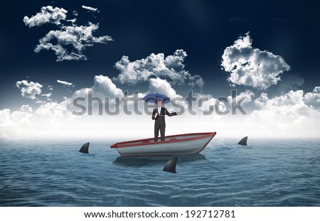 Peaceful businessman holding blue umbrella against sharks circling small boat in the sea
