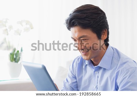 Happy man sitting on couch using tablet pc at home in the living room