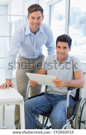 Casual businessman in wheelchair smiling at camera with colleague in the office