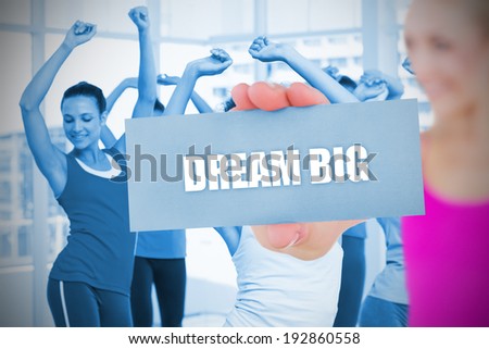 Fit blonde holding card saying dream big against fitness class in gym
