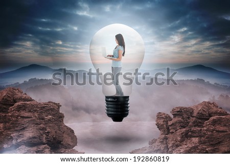 Woman holding laptop in light bulb against rocky landscape