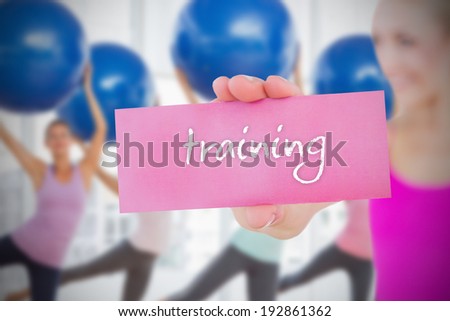 Fit blonde holding card saying training against fitness class in gym