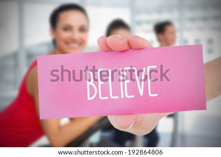 Woman holding pink card saying believe against fitness class in gym