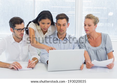 Casual business team working together at desk using laptop in the office