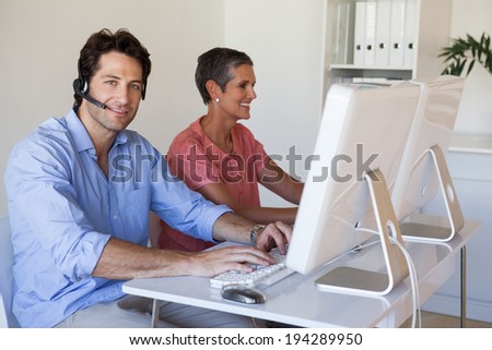 Casual business team working at desk using computers with man smiling at camera in the office