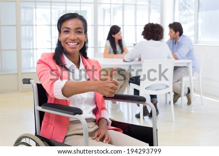 Attractive businesswoman in wheelchair gives thumbs up to camera in the office