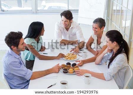 Business people chat while eating muffins and drinking coffee in the office