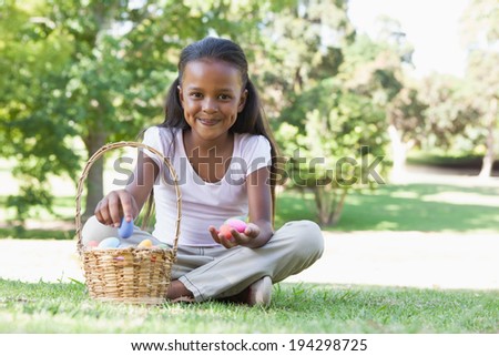 Little girl sitting on grass counting easter eggs smiling at camera on a sunny day