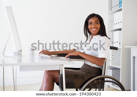 Smiling businesswoman in wheelchair working at her desk in her office