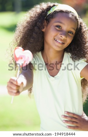 Young girl holding a heart lollipop in the park on a sunny day