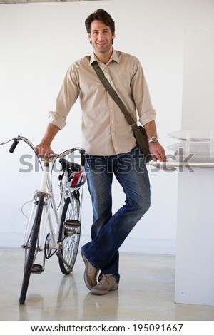 Casual businessman standing with his bike smiling at camera in the office