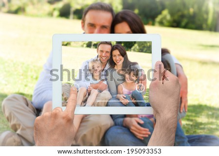 Hand holding tablet pc showing family sitting in the park