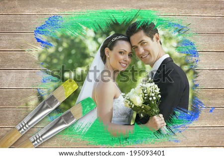 Composite image of newlyweds smiling at camera with paintbrush dipped in green against wooden surface with planks