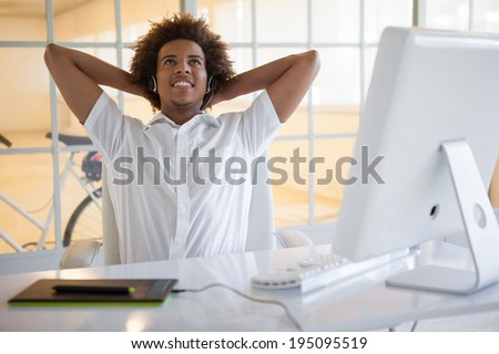 Smiling young businessman using digitizer and headset at desk in his office