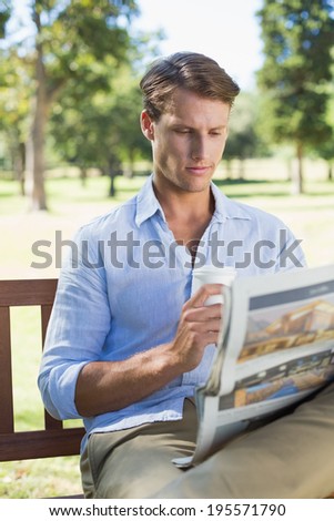 Man sitting on park bench drinking coffee and reading paper on a sunny day