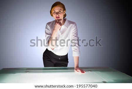 Redhead businesswoman standing and thinking by a desk on shadow background