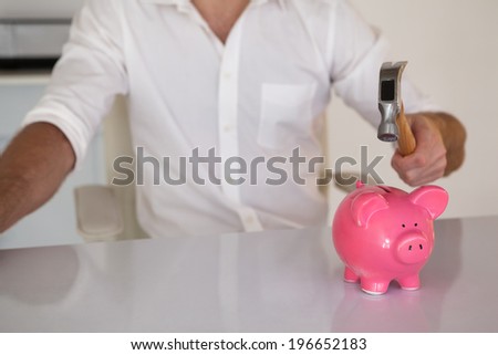 Casual businessman breaking piggy bank with hammer in his office