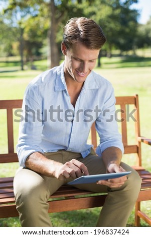 Smiling man sitting on park bench using tablet on a sunny day