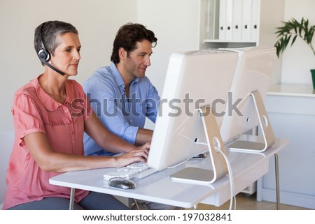 Casual business team working at desk using computers with woman using headset in the office