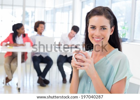 Attractive businesswoman drinking hot beverage with colleagues in background in the office