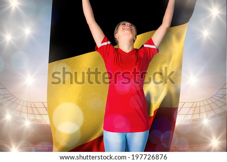 Cheering football fan in red holding belgium flag against large football stadium under blue sky