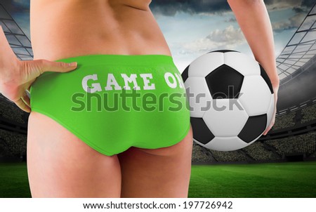 Fit girl in green bikini holding football against large football stadium with lights