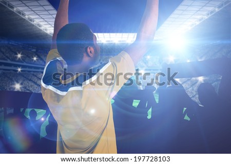 Cheering football fan in yellow jersey against large football stadium with lights