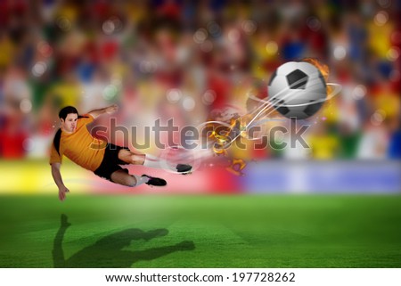 Football player in orange kicking against blurry football pitch with crowd