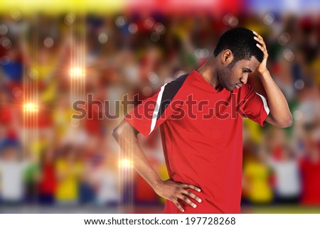 Disappointed football fan looking down against blurry football pitch with crowd