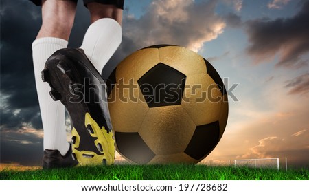 Composite image of football boot kicking huge gold ball against green grass under blue and orange sky