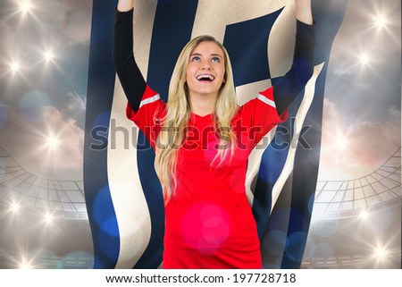 Cheering football fan in red holding greece flag against large football stadium under cloudy blue sky