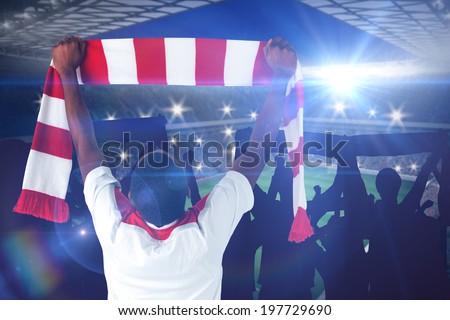 Happy football fan waving scarf against large football stadium with lights