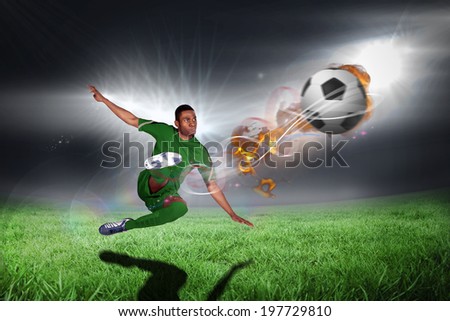 Football player in green kicking against football pitch under bright lights