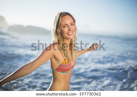 Content blonde standing on the beach in bikini with arms out on a sunny day