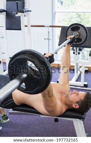 Shirtless bodybuilder lifting heavy barbell weight lying on bench at the gym