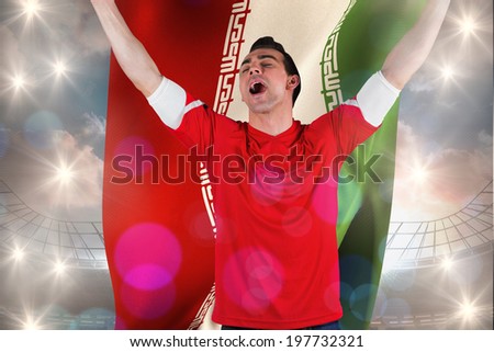 Excited football fan cheering holding iran flag against large football stadium under cloudy blue sky