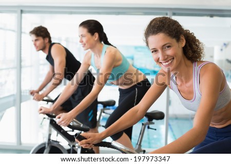 Fit people in a spin class with woman smiling at camera at the gym